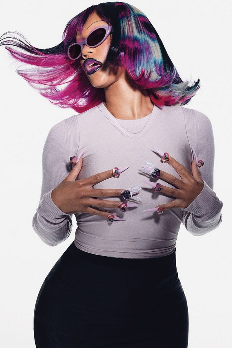 Person with pink black and white vibrant wig and vibrant makeup wearing a light gray sweater and black pants.