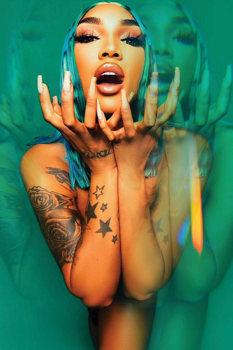 Person with tattoos and colorful nails against a green background. They are wearing a blue black and green painted wig.