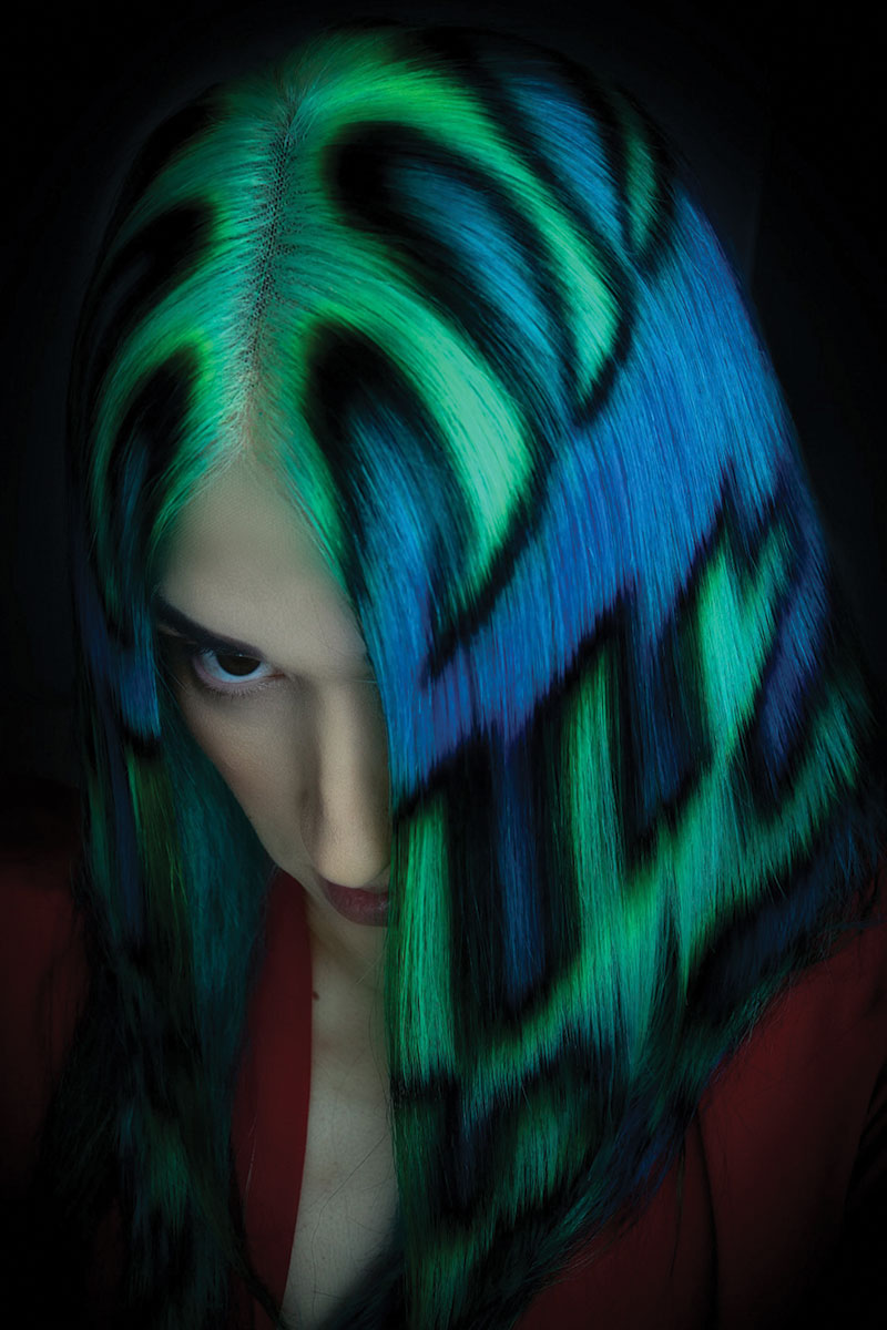 Person with vibrant green and blue painted wig against a dark background