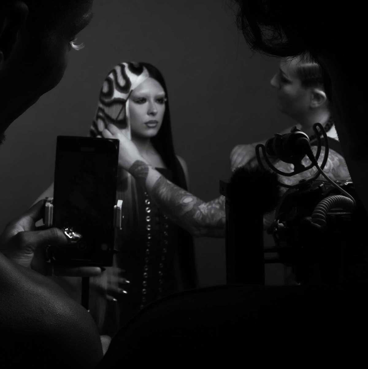 black and white image of behind the scenes of a photo shoot. two individuals take photos while Shannon adjusts the fire wig on a model