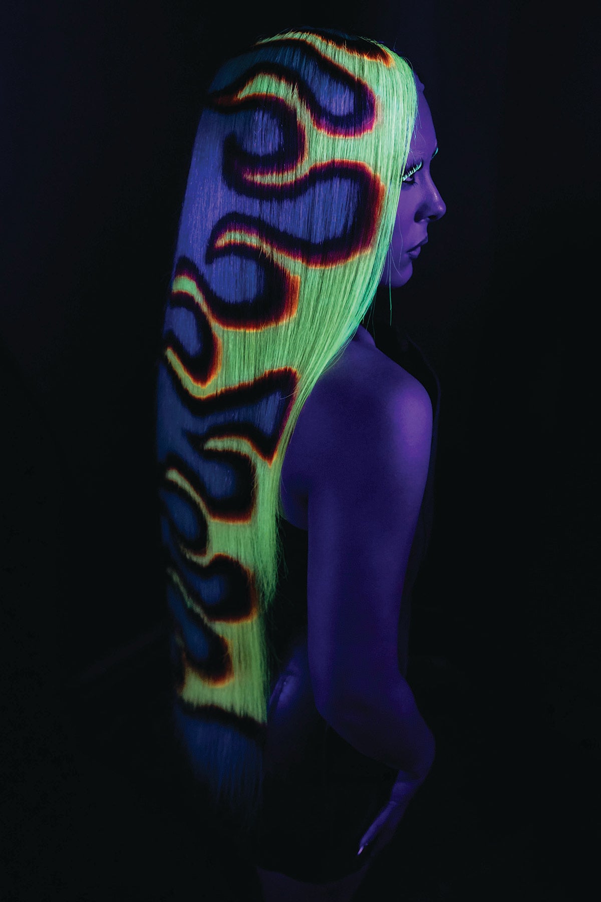 a back side view of a model in a waist length fire wig, glowing under black light