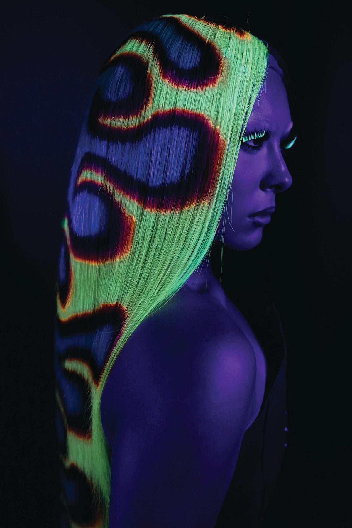 a side view of a model wearing a fire wig, glowing under black light