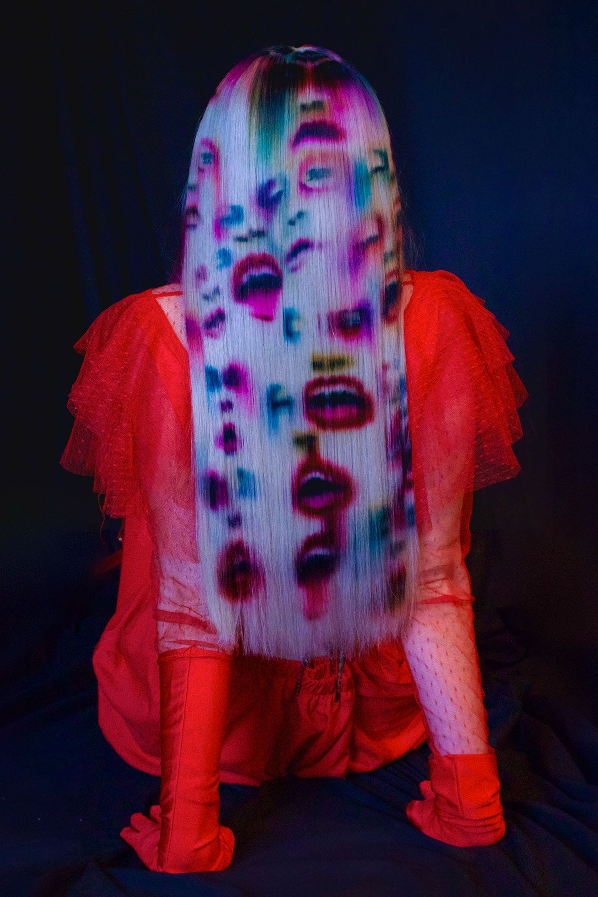 A back view of a model in red clothing wearing a white blonde wig. Faces and mouths are painted into the wig