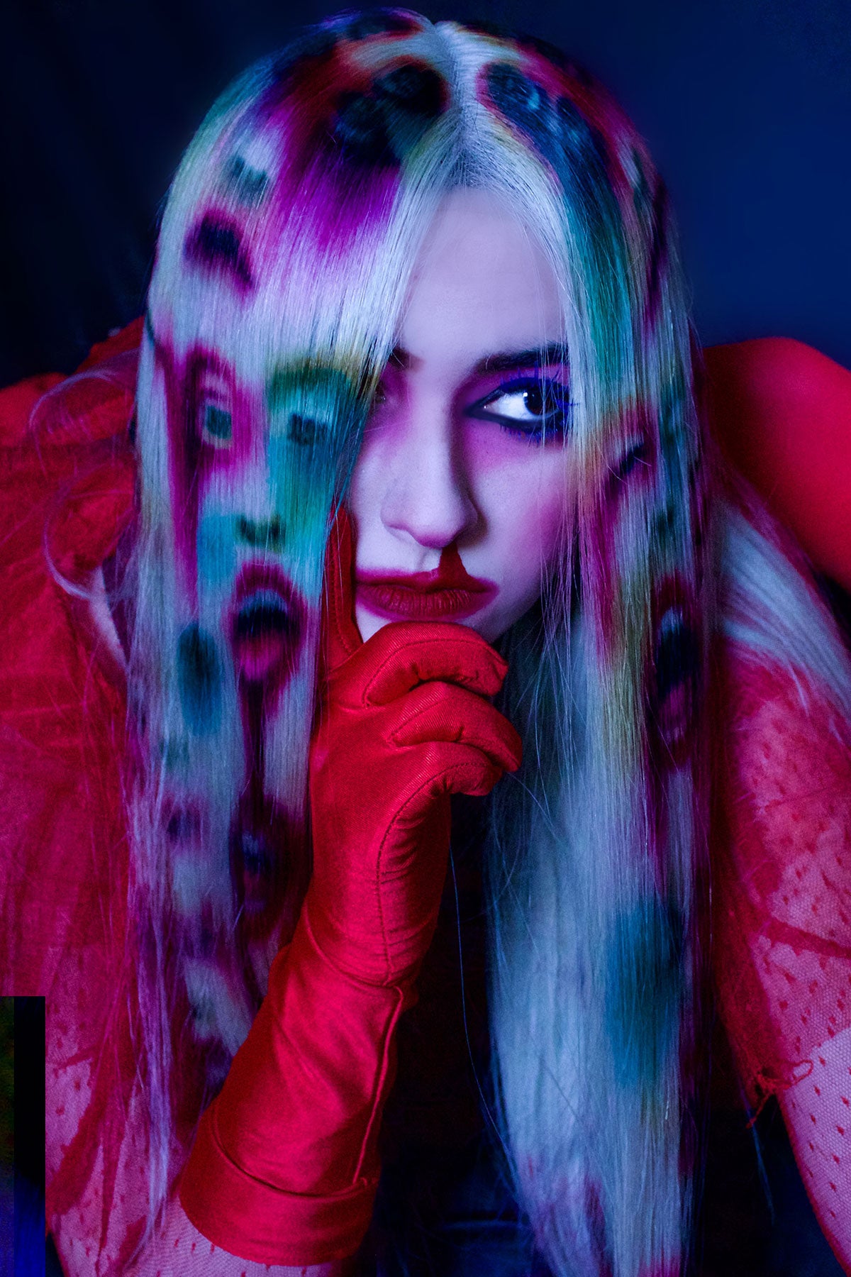 A front view of a model in red clothing wearing a white blonde wig. Faces and mouths are painted into the wig