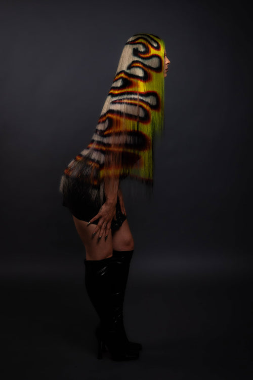 a side view of a model in a black dress wearing a black yellow and red fire wig