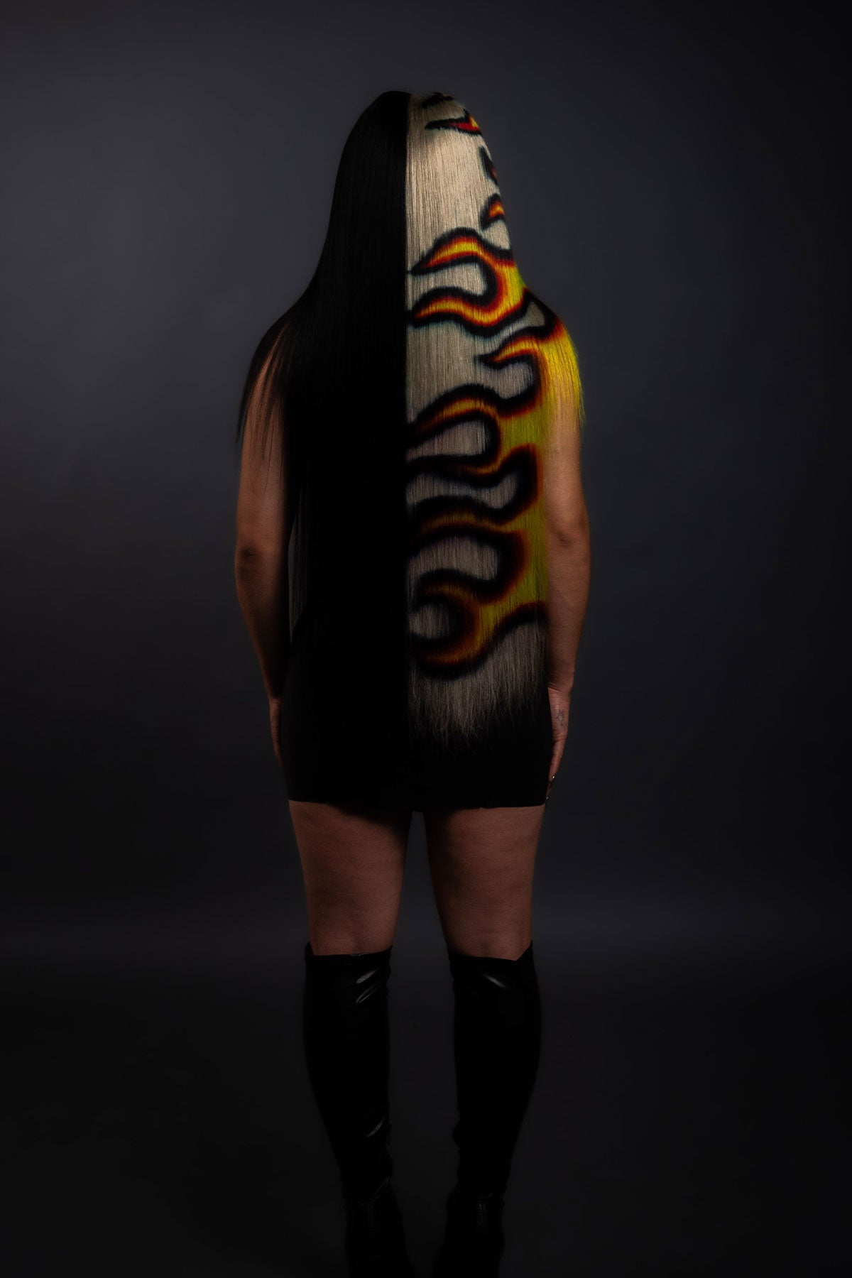 a back view of a model in a black dress wearing a black yellow and red fire wig