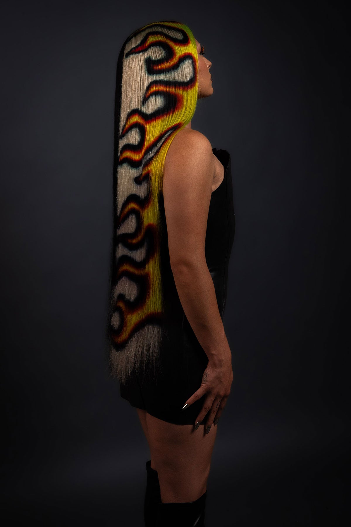 a side view of a model in a black dress wearing a black yellow and red fire wig