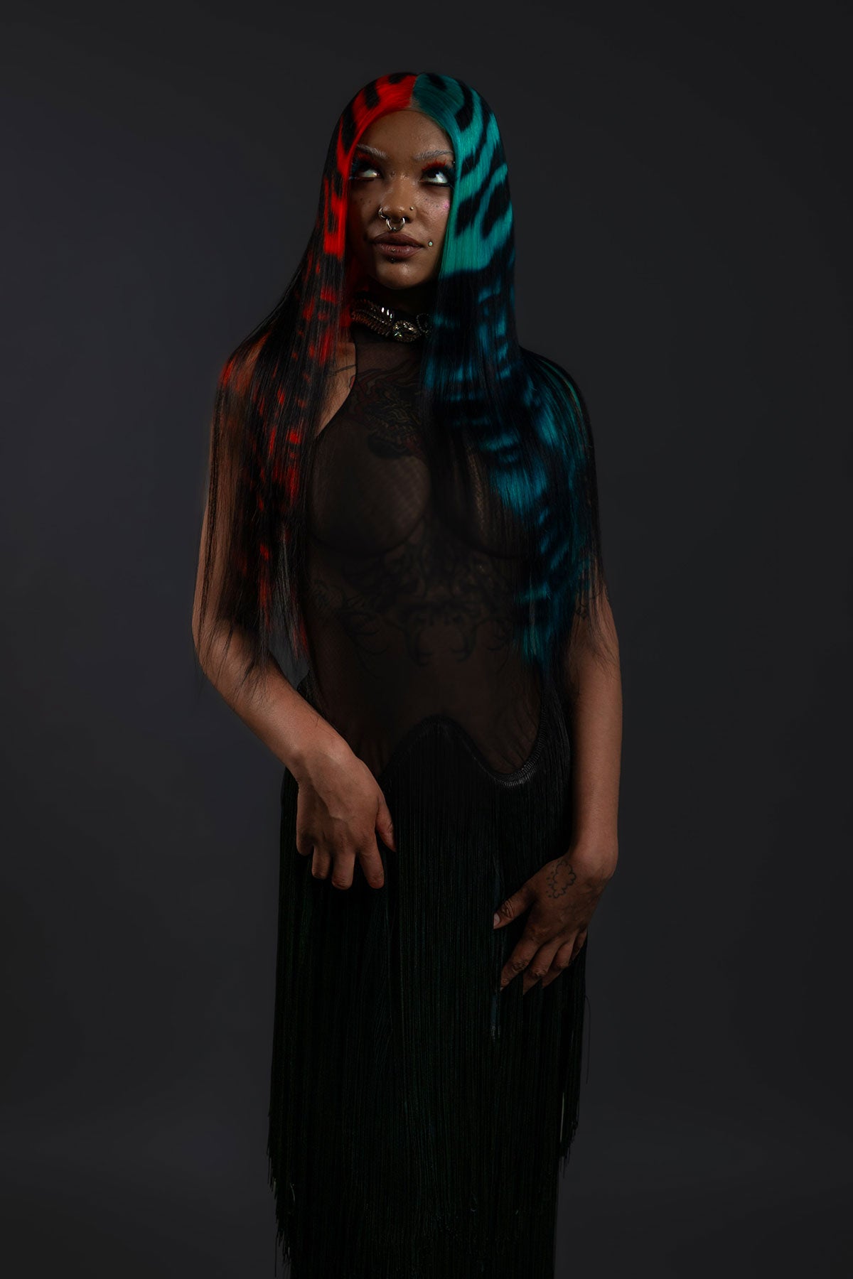 a front view of a model wearing a black outfit and a black waist length wig with blue and red faces painted into it