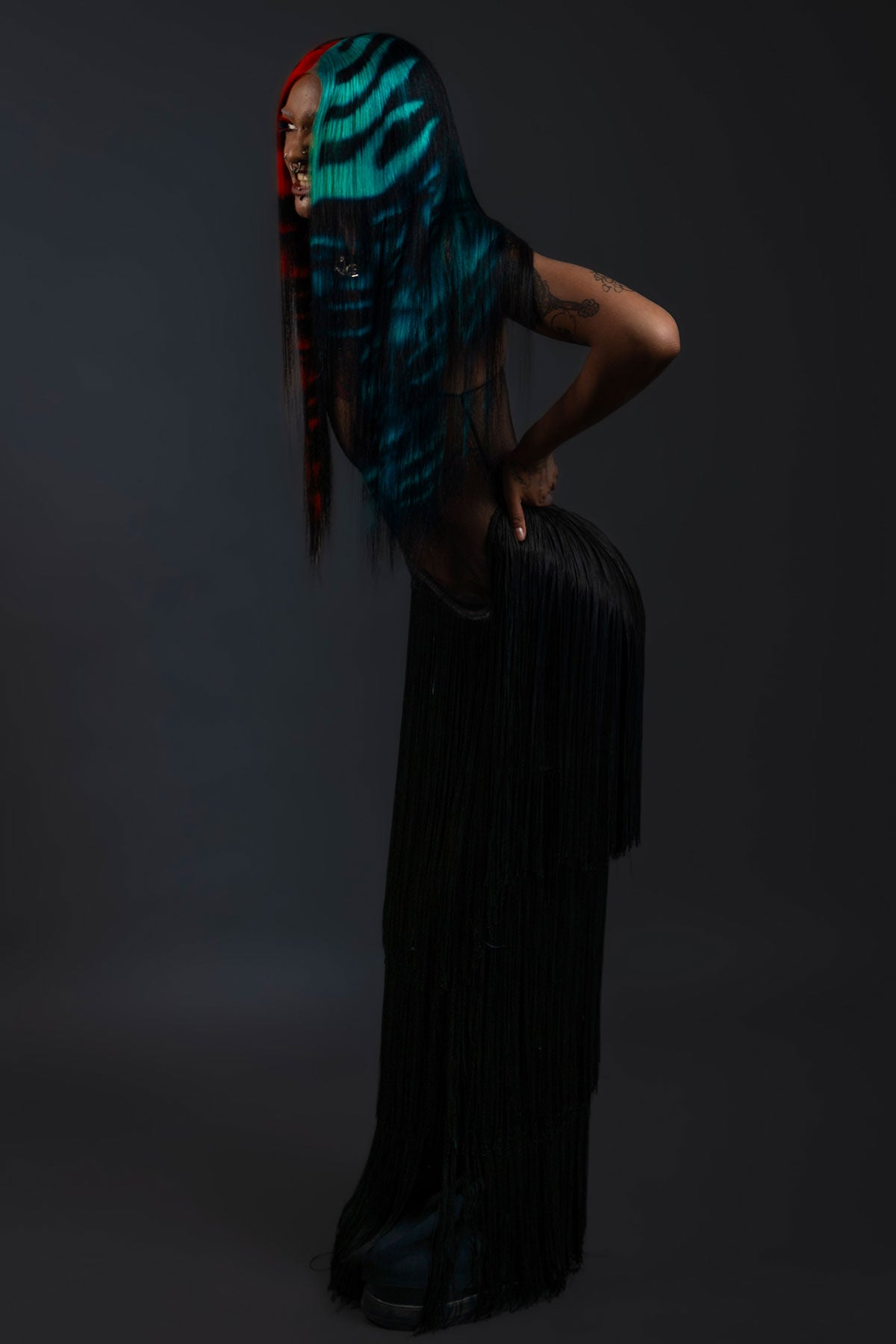 a side view of a model wearing a black outfit and a black waist length wig with blue and red faces painted into it