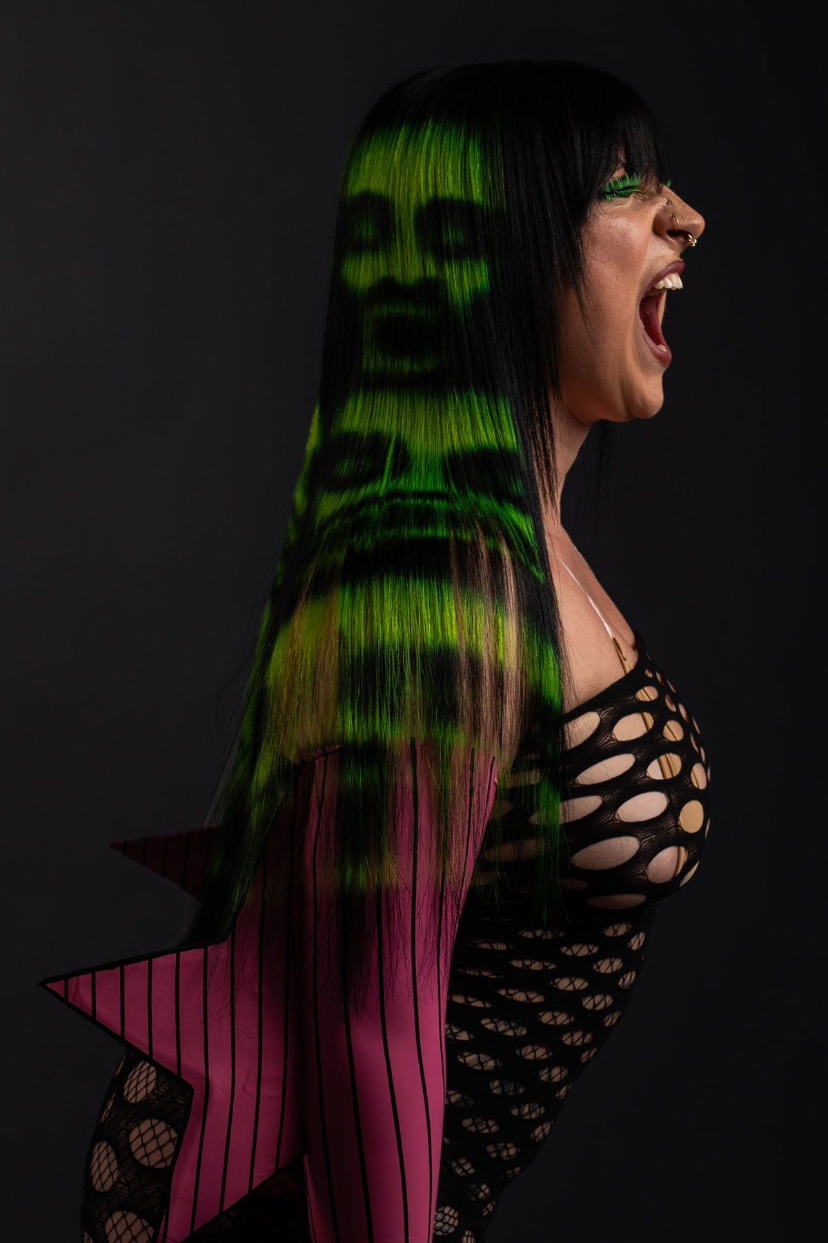 a side view of a model wearing a black and green zombie wig and a fishnet dress 