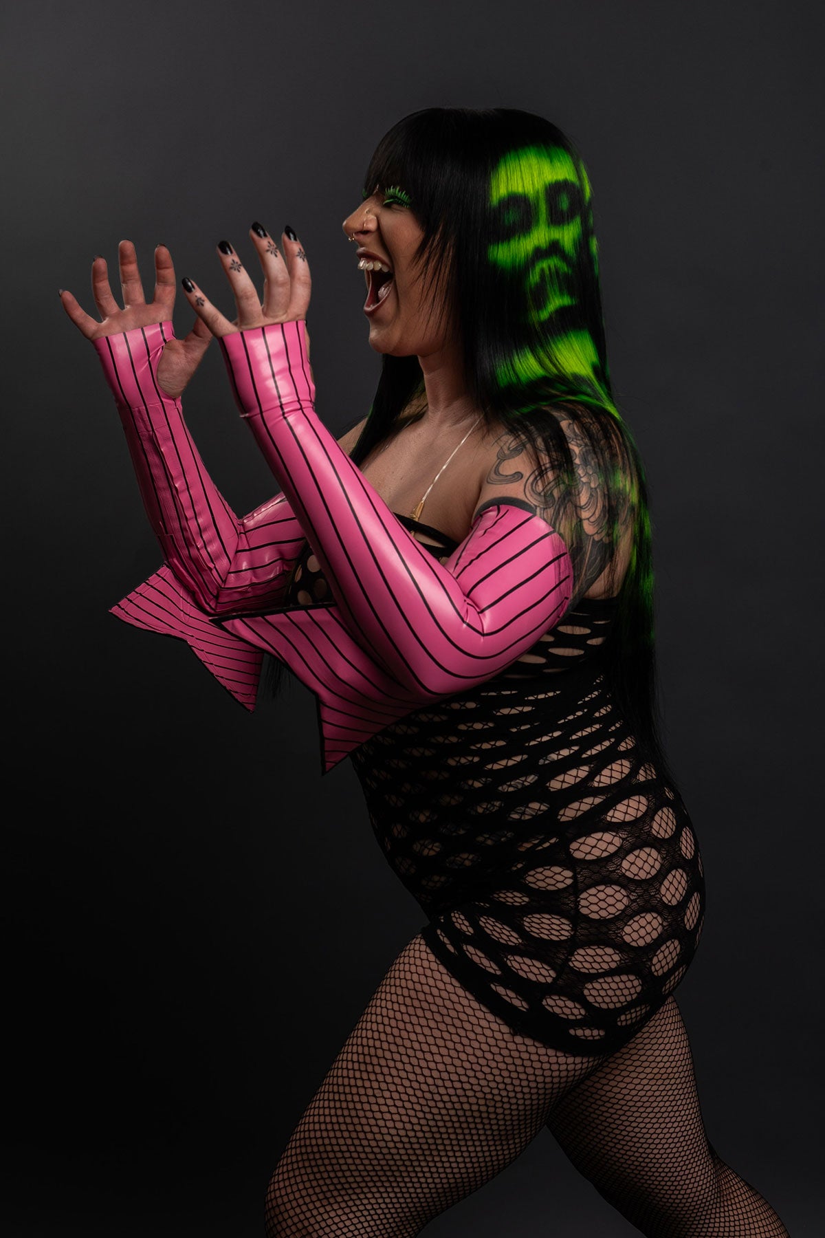 a side view of a model wearing a black and green zombie wig and a fishnet dress with black boots