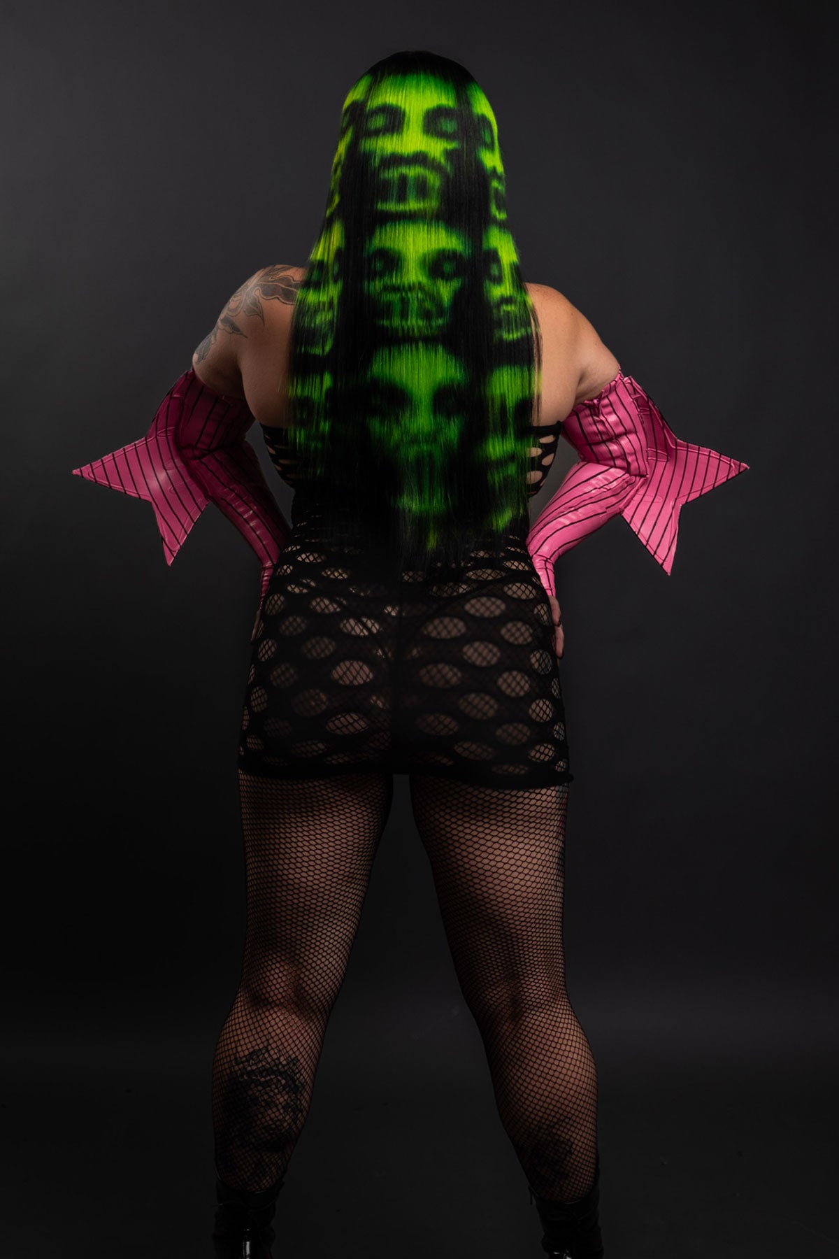 a back view of a model wearing a black and green zombie wig and a fishnet dress with black boots