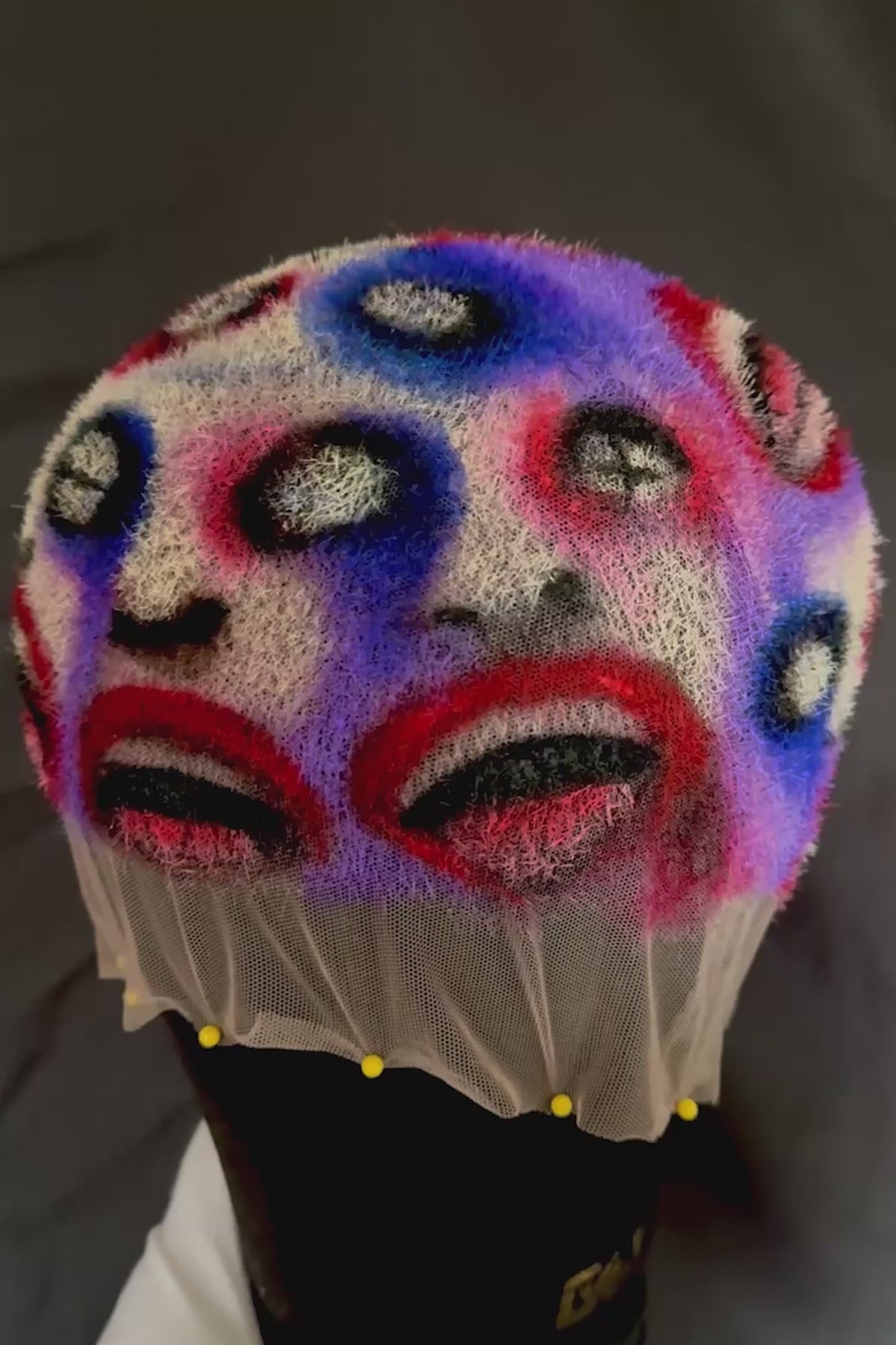 a colorful wig with faces painted into it rotating on a mannequin and then being worn by a model